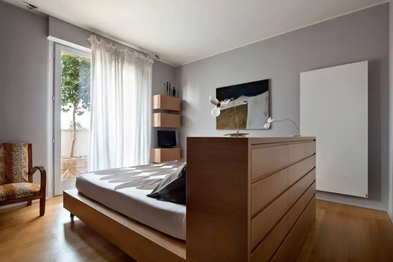 Un moderno **letto in mezzo alla stanza**, con un copriletto a motivi floreali, accanto a una poltrona leopardata e una cassettiera in legno.