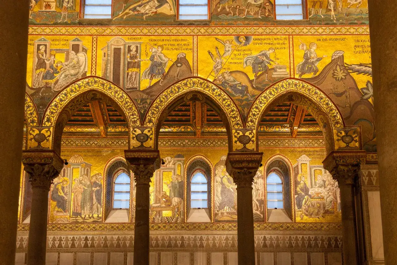 Mosaici dorati narrano storie bibliche, un capolavoro di arte siciliana. Colonne e archi incorniciano scene sacre, un tesoro bizantino.