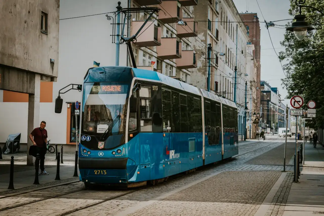 Błękitny tramwaj 23 Wrocław na brukowanej ulicy, obok kamienic.