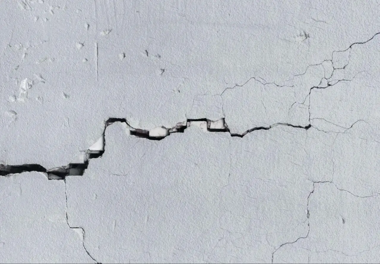 Una grieta profunda atraviesa una pared de estuco blanco, mostrando el interior dañado. Es necesario sanear pared para repararla.