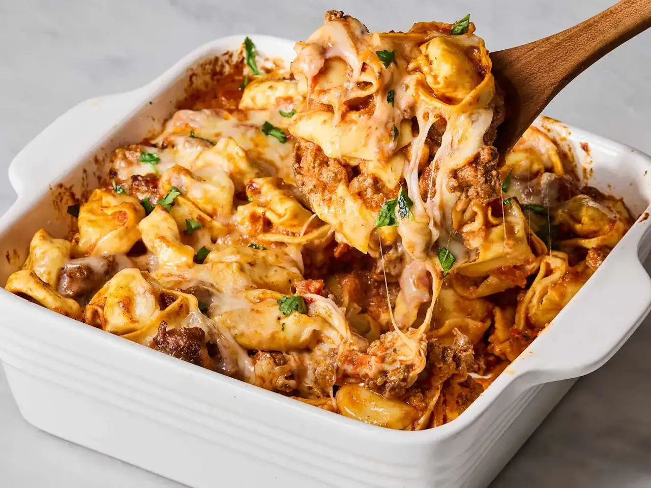 Herzhaftes Auflaufgericht mit Tortellini, Hackfleisch und geschmolzenem Käse, garniert mit Petersilie. Ein köstliches Beispiel für Tortellini-Gerichte.