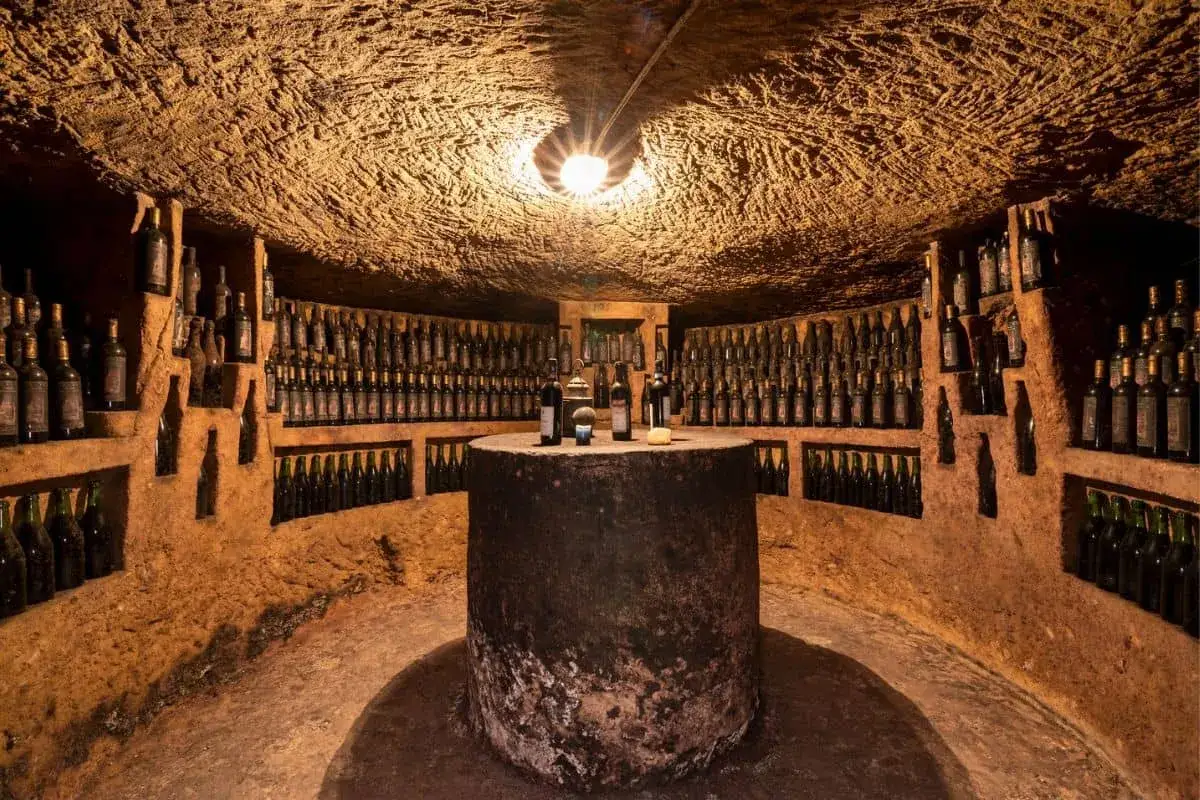 Cantina scavata nella roccia, con scaffali pieni di bottiglie di vino, perfetta per un weekend nel Monferrato.