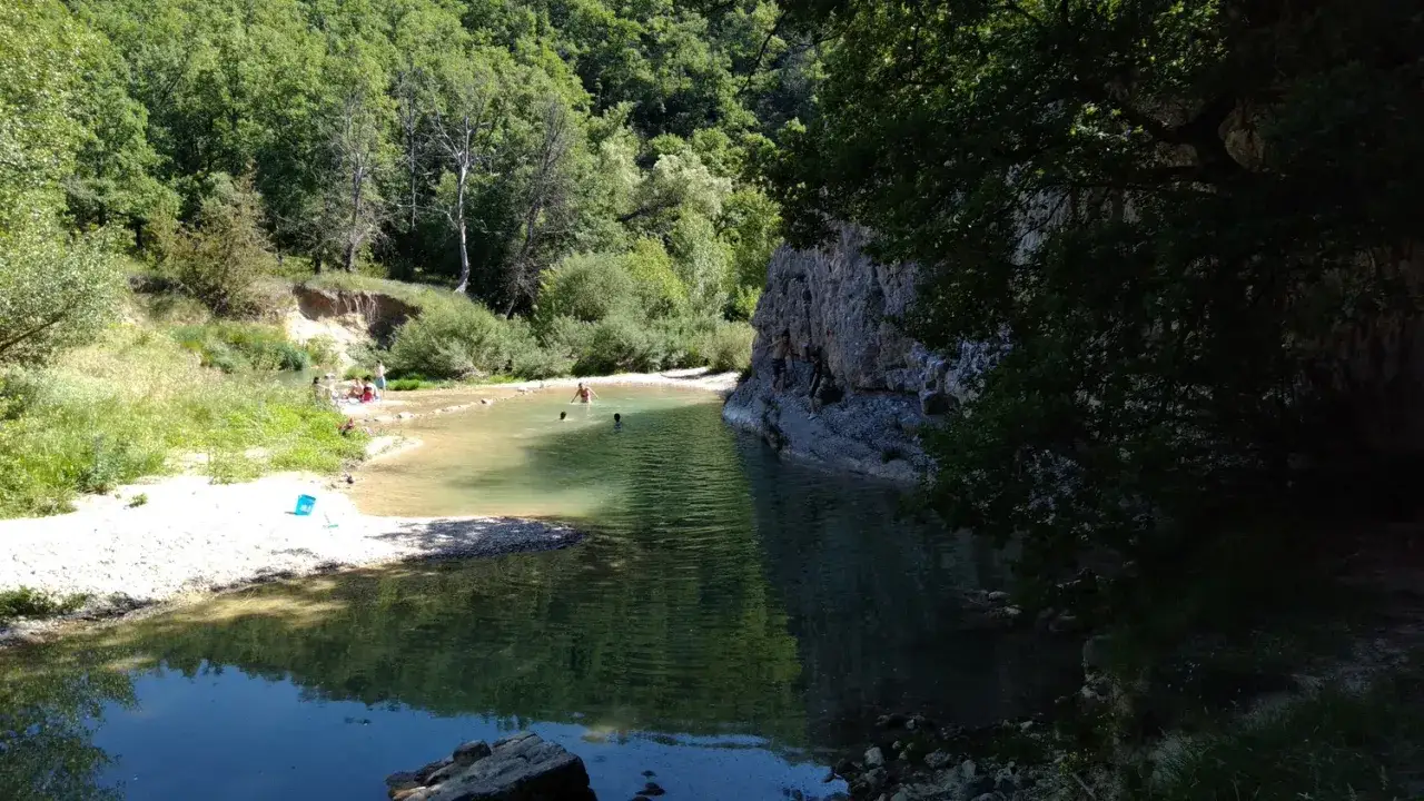 Des baigneurs profitent d'une rivi&egrave;re aux eaux claires pr&egrave;s du rocher des abeilles, certains grimpent sur la paroi rocheuse.