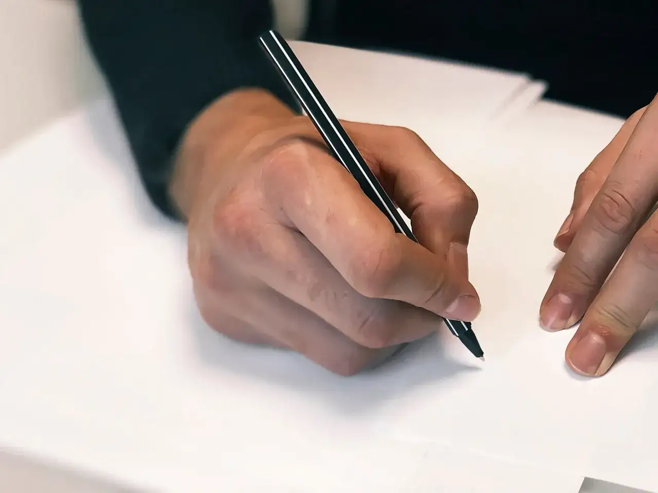 Dłoń pisze długopisem. Zastanawiasz się, jak długo jest ważny testament własnoręczny? Pamiętaj o jego prawidłowym sporządzeniu.