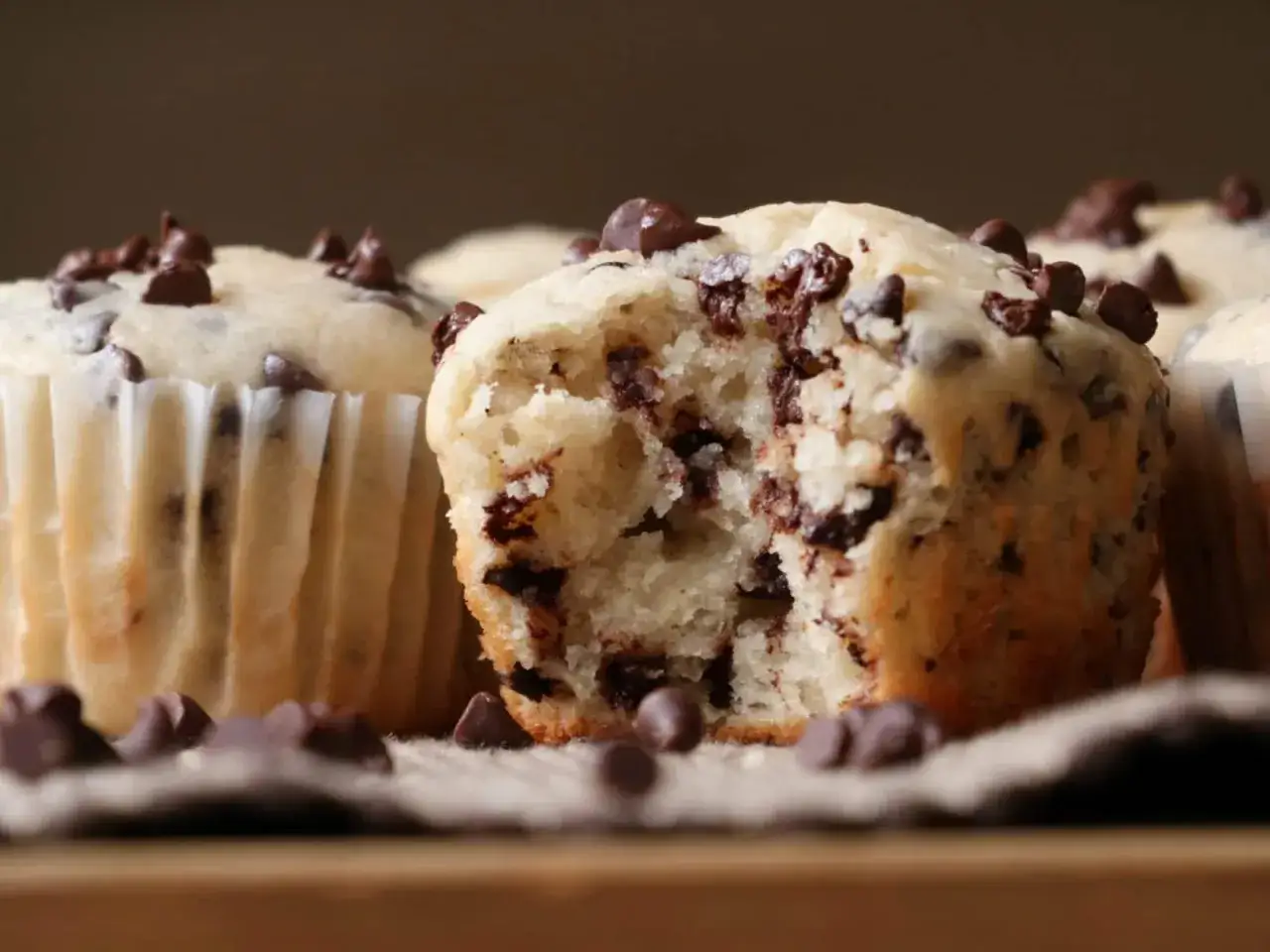 Saftige Schokomuffins, perfekt für ein schnelles schokomuffins rezept. Ein Muffin ist angeknabbert und zeigt die vielen Schokostückchen.