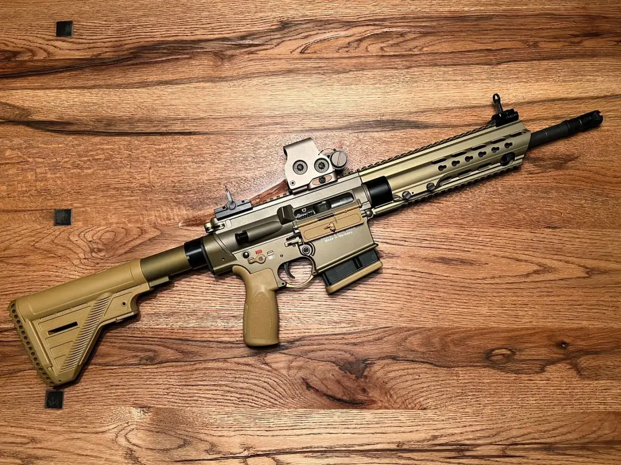 Un fusil MR 308, de couleur sable, repose sur un fond en bois.