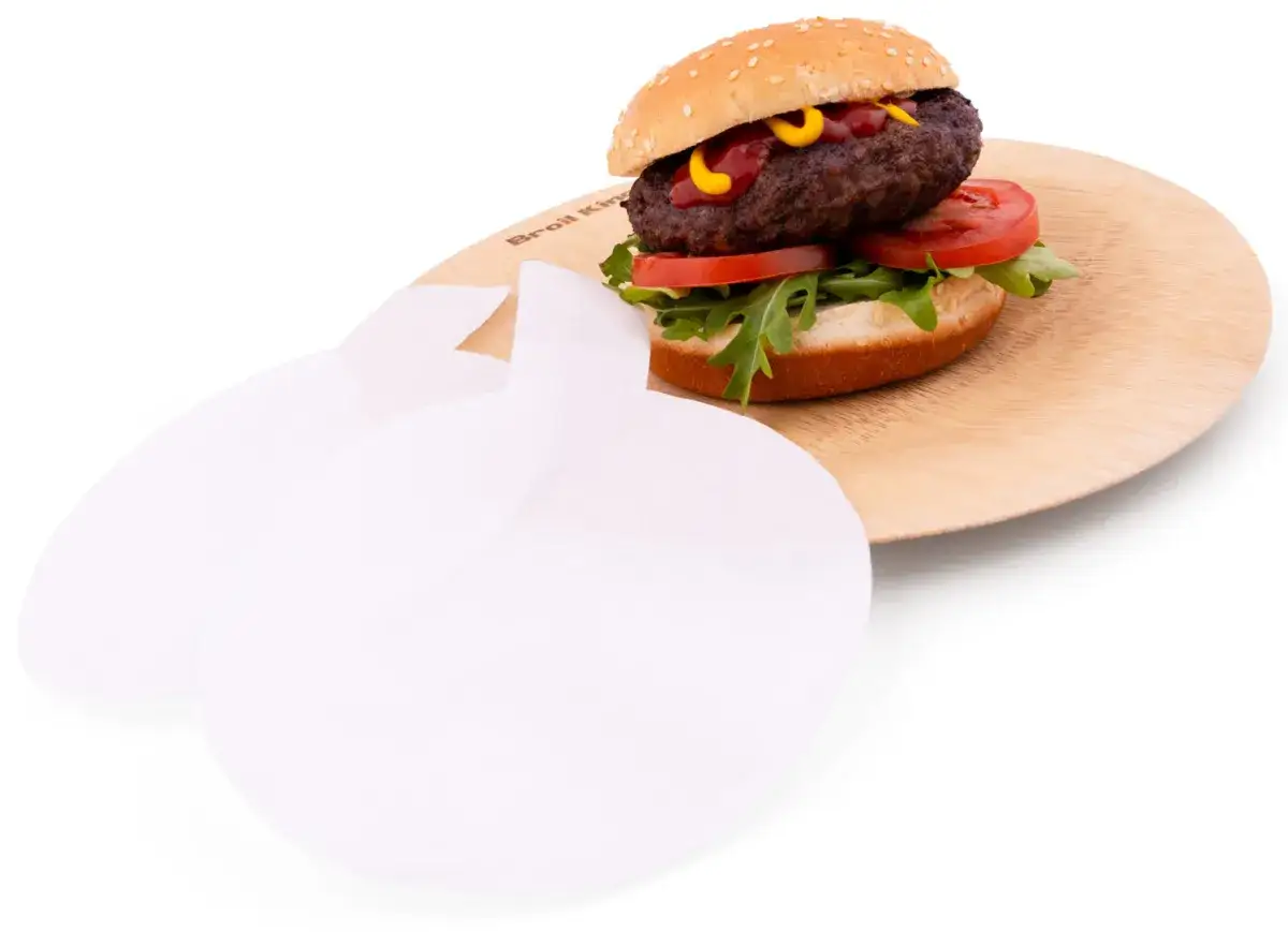 Pyszny burger na drewnianej desce, obok białe papierki, które mogą służyć jako pomoc przy formowaniu mięsa za pomocą praski do burgerów.