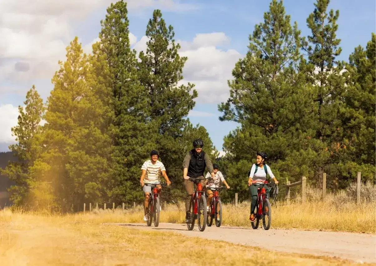A family enjoys a scenic ride on electric bikes, experiencing the benefits of effortless exploration and outdoor fun amidst tall trees and a sunny sky.