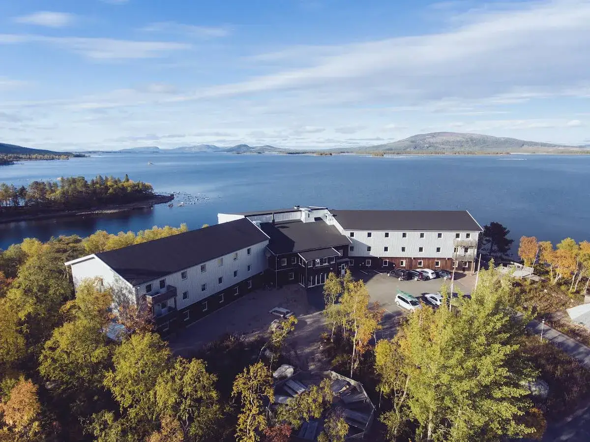 Vandrarhem Arjeplog vid en stor sjö, omgivet av höstfärgad skog.