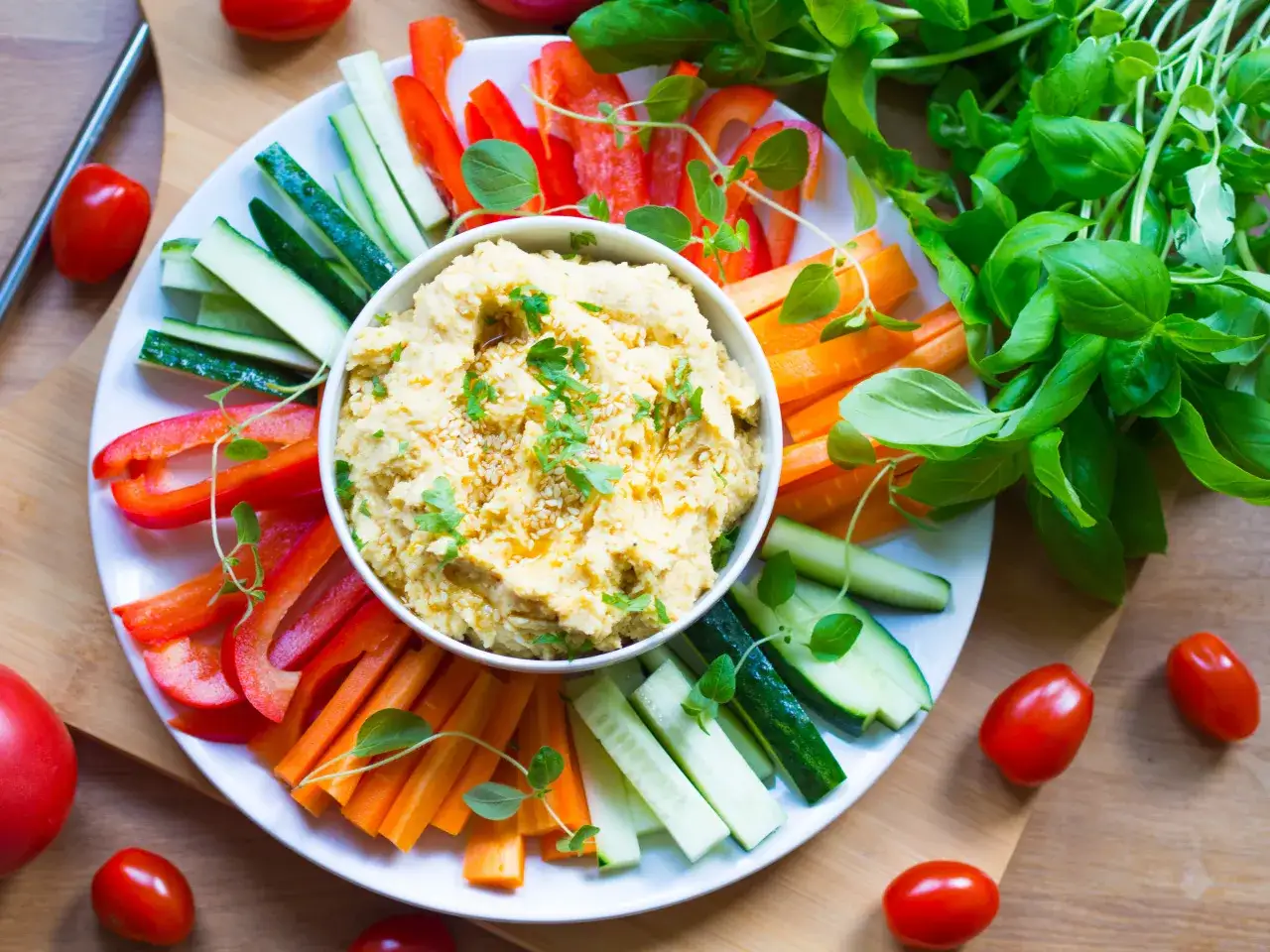 Pyszny hummus z ciecierzycy, podany z kolorowymi warzywami: papryką, ogórkiem i marchewką. Idealna przekąska, co to jest hummus?