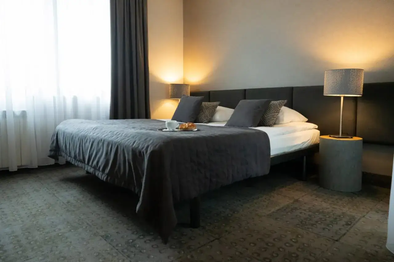 Przytulny pokój w hotelu Perła Kraków. Łóżko z pościelą, taca ze śniadaniem i lampka nocna.