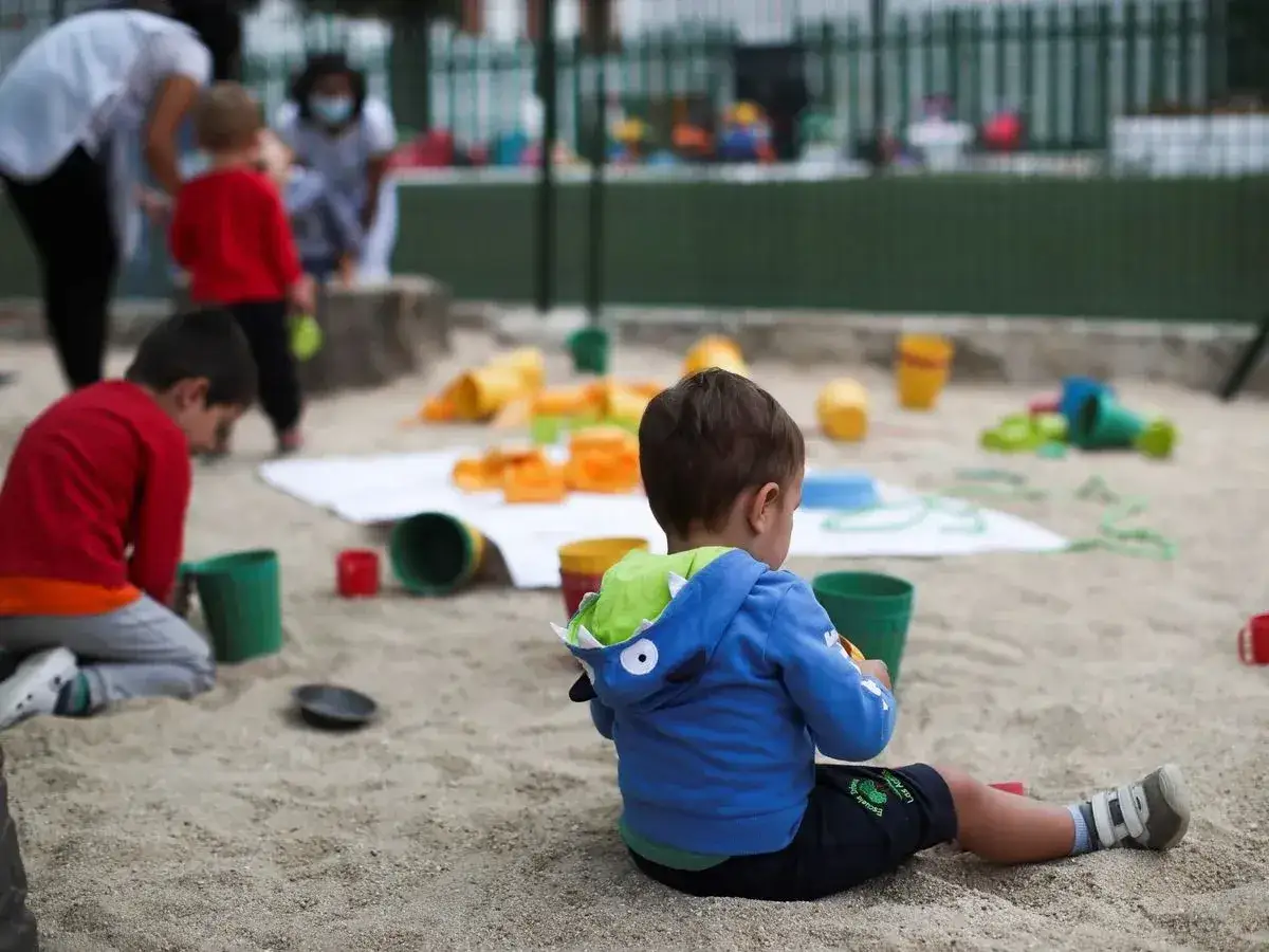 Niños jugando en la arena, una escena que muestra a qué edad se empieza la guardería, con educadores supervisando.