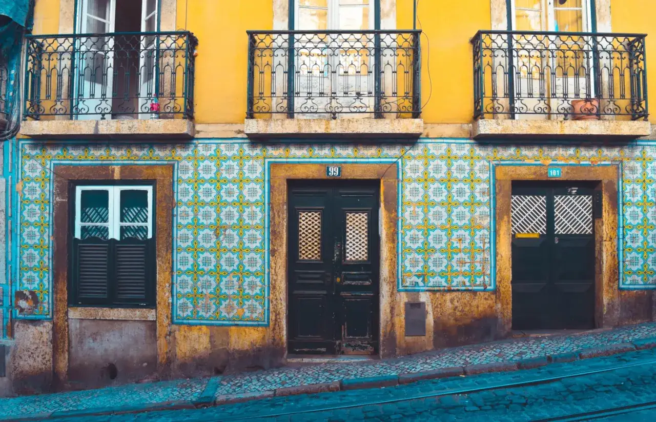 Fasada kamienicy z ż&oacute;łtym tynkiem, ozdobiona azulejos, balustradami i drzwiami. To kwintesencja kultury Portugalii.