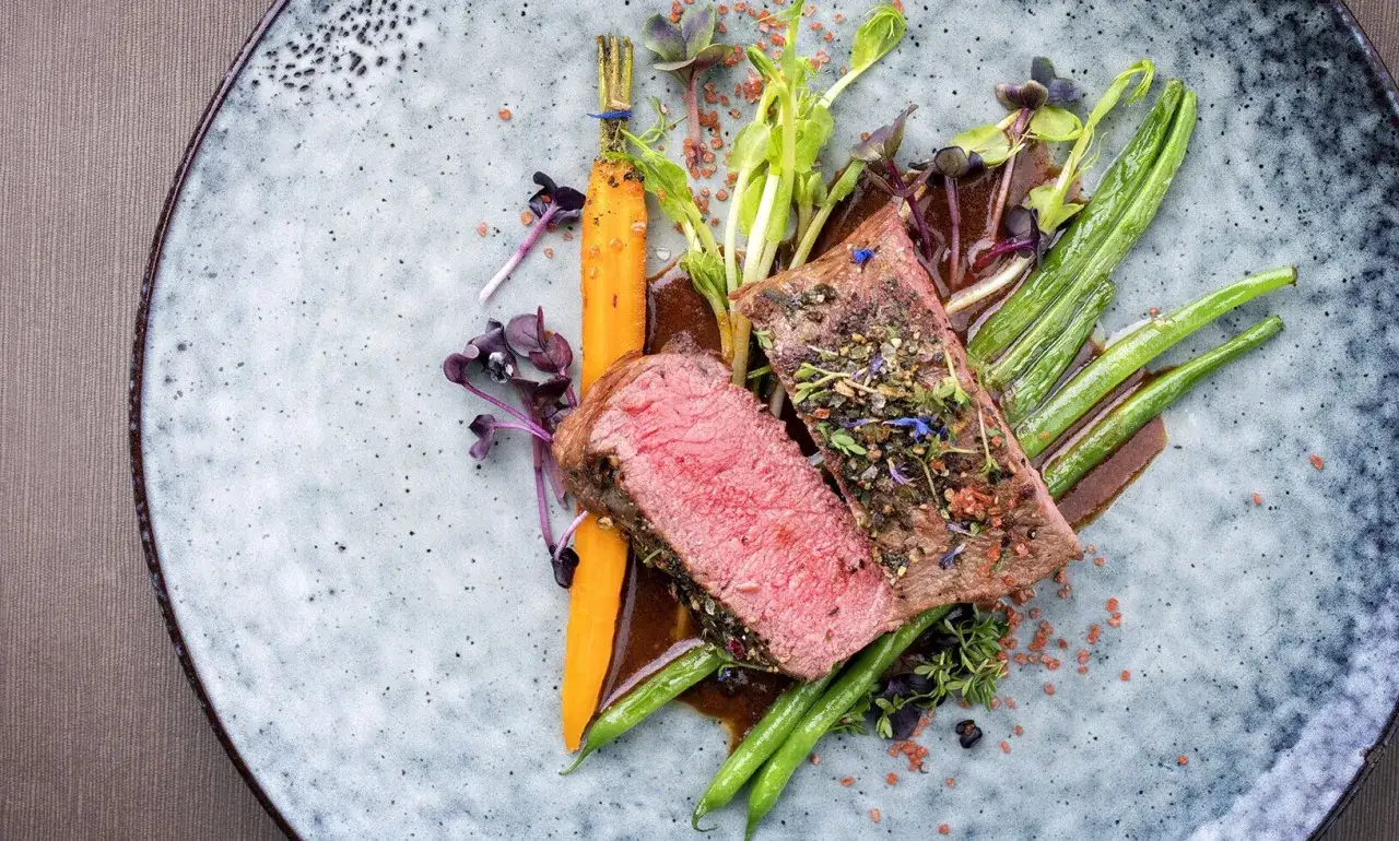 Un v&eacute;ritable coup de food : un steak saignant, carottes, haricots verts et pousses croquantes sur une assiette textur&eacute;e.