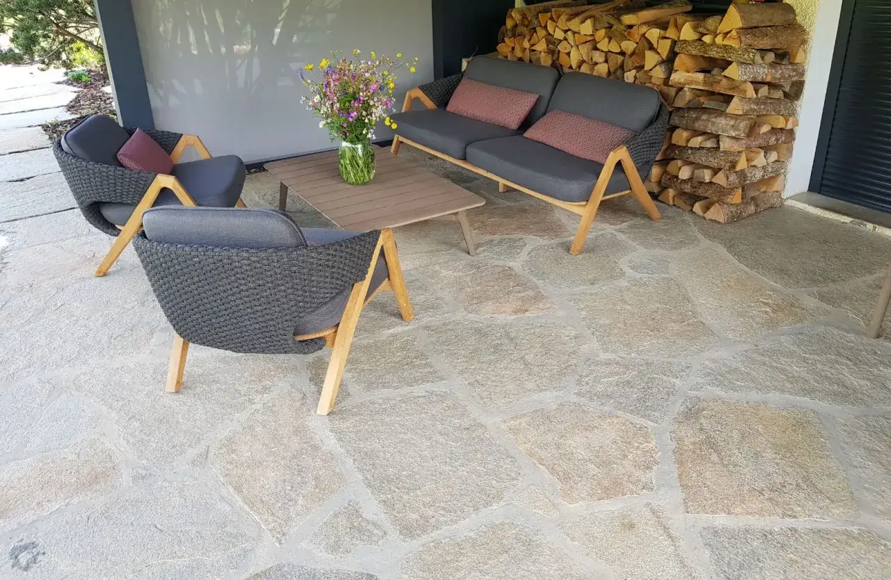 Terrasse en pierre naturelle extérieure, traitée avec un imperméabilisant pour une protection durable. Mobilier de jardin confortable et bois de chauffage empilé.