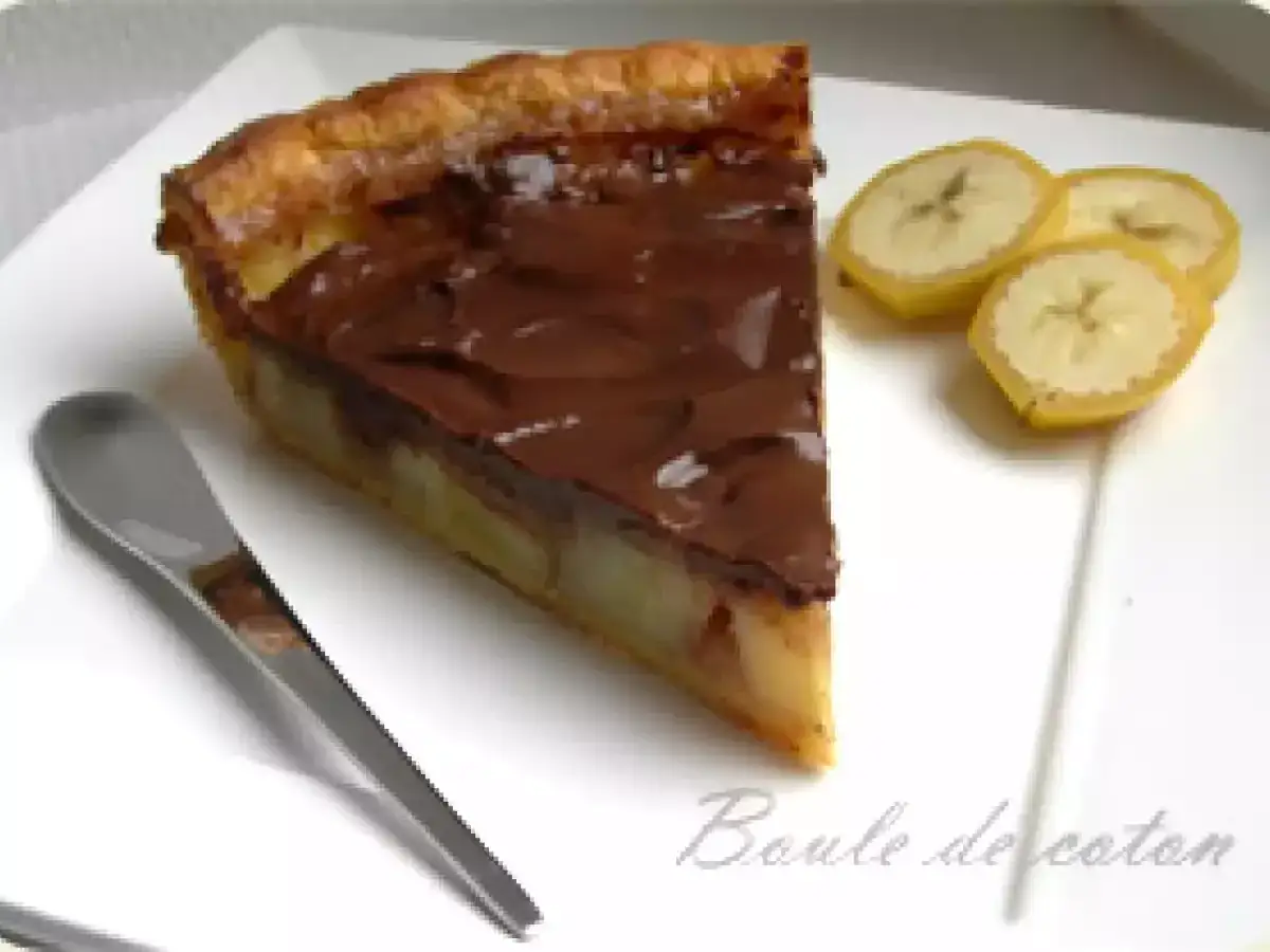 Tranche de tarte banane chocolat, garnie de chocolat fondant et accompagnée de rondelles de banane. Une cuillère est posée à côté.