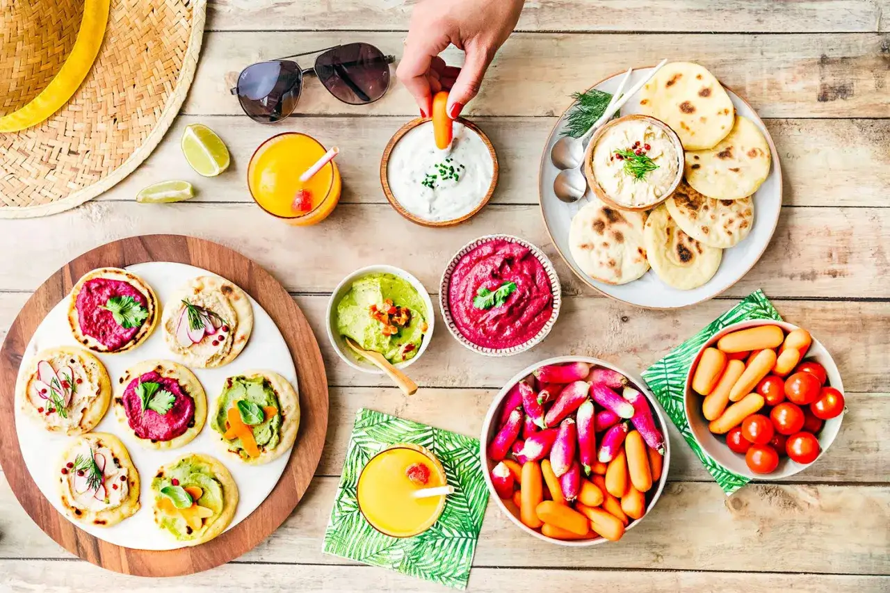 Un ap&eacute;ro dr&ocirc;le avec des mini-pains garnis de houmous, guacamole et betterave, accompagn&eacute; de crudit&eacute;s et jus d'orange.