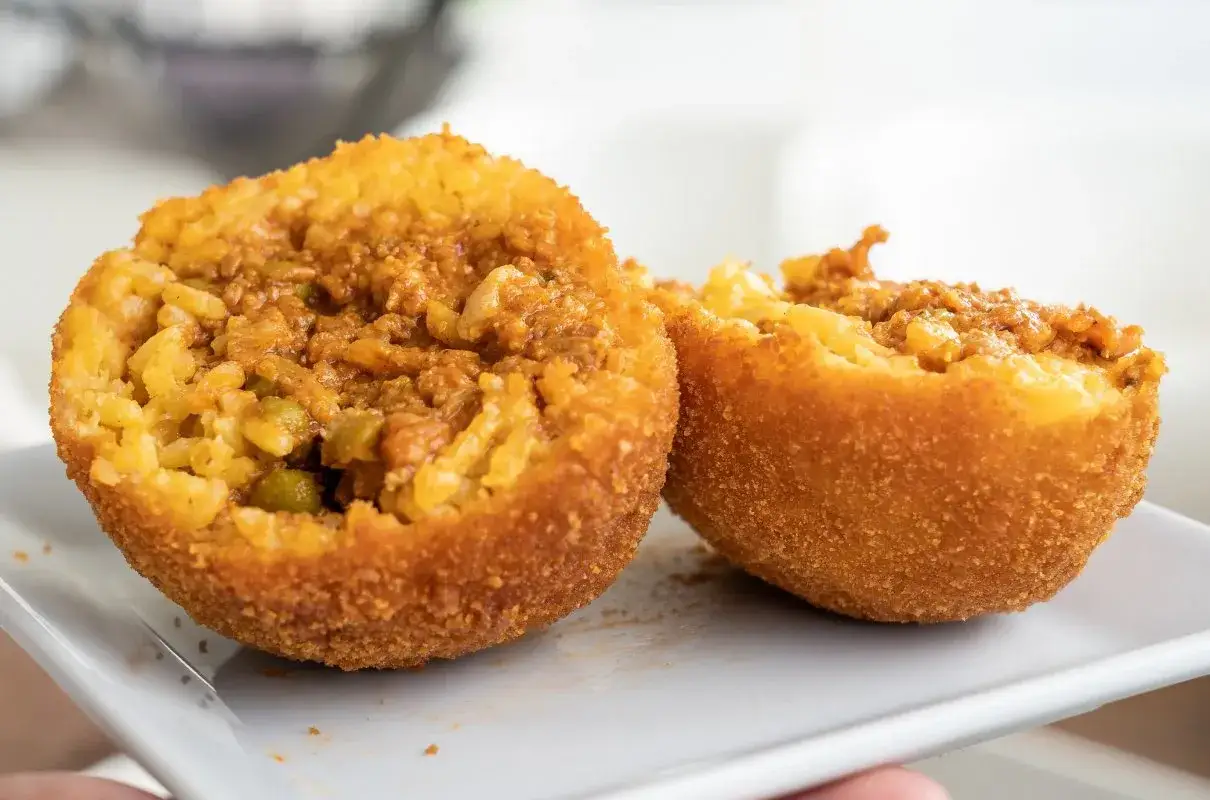 Dwa chrupiące arancini, przekrojone na pół, ukazują ryż z mięsem i groszkiem. To właśnie arancini co to za przysmak!
