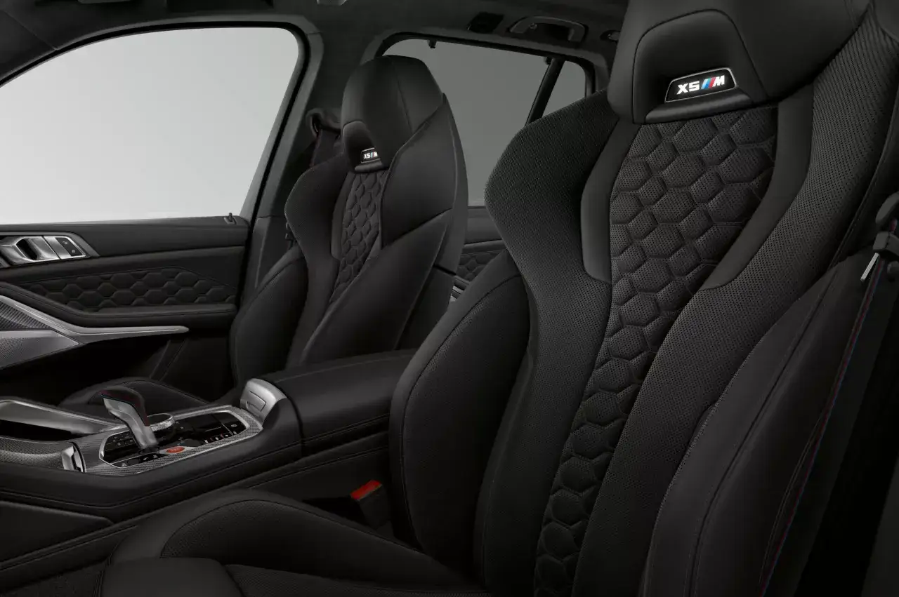 Wnętrze BMW X5 M Competition: czarne, sportowe fotele z perforacją i pikowaniem, emblemat X5/M na zagłówku, dźwignia zmiany biegów.