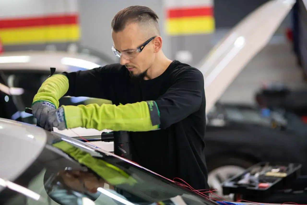 Mechanik w okularach i rękawicach montuje elementy do przedniej szyby, pokazując jak zrobić podgrzewanie przedniej szyby.