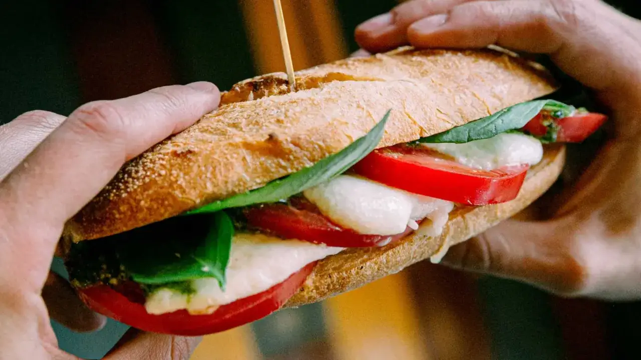 Chleb włoski z mozzarellą, pomidorami i bazylią, trzymany w dłoniach. Pyszny smak lata.