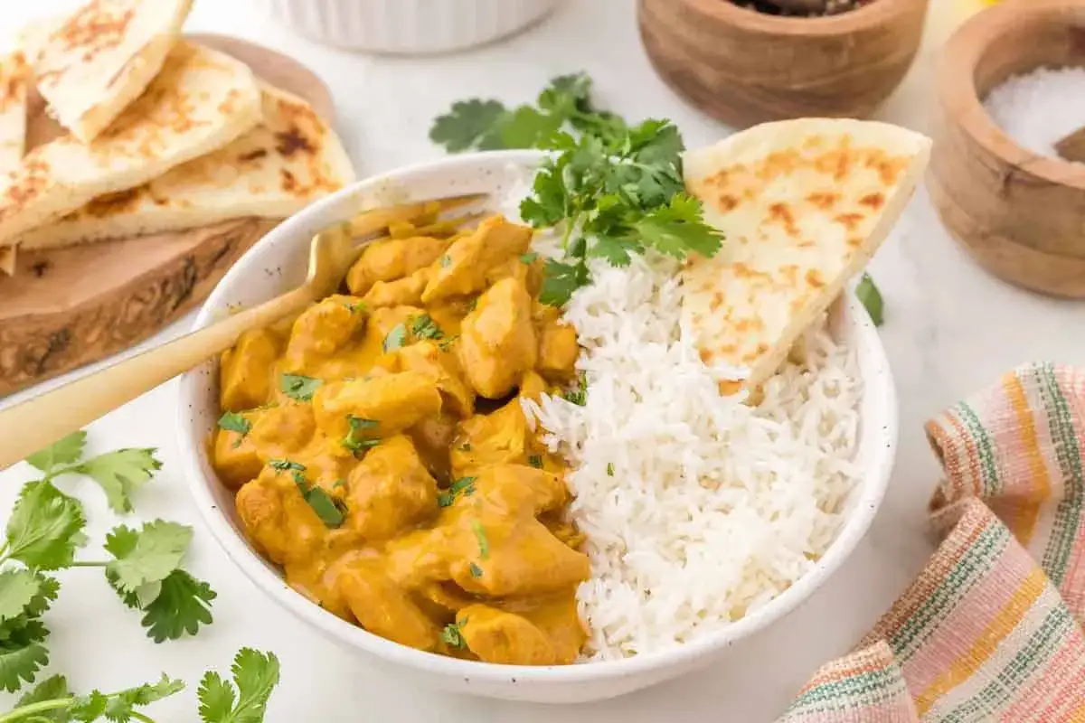 Cremiges Chicken Korma mit Basmatireis, Naan-Brot und frischem Koriander. Ein köstliches indisches Gericht.