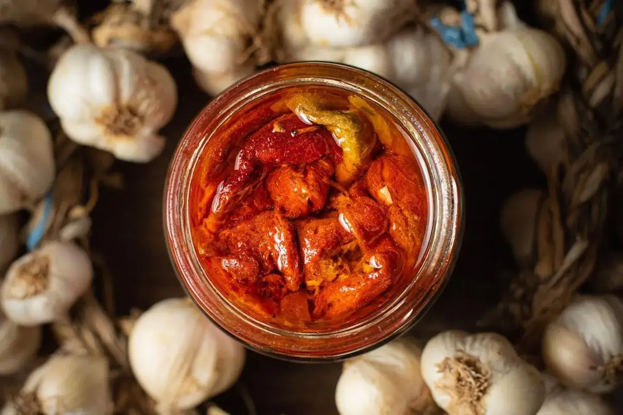 Słoik z suszonymi pomidorami w oleju, otoczony czosnkiem. Ajvar do czego? Do kanapek, sosów, jako dodatek do dań.