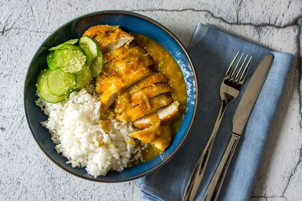 Chrupiące katsu z kurczaka w sosie curry, podane z ryżem i plasterkami ogórka. Pyszny obiad gotowy do spożycia!