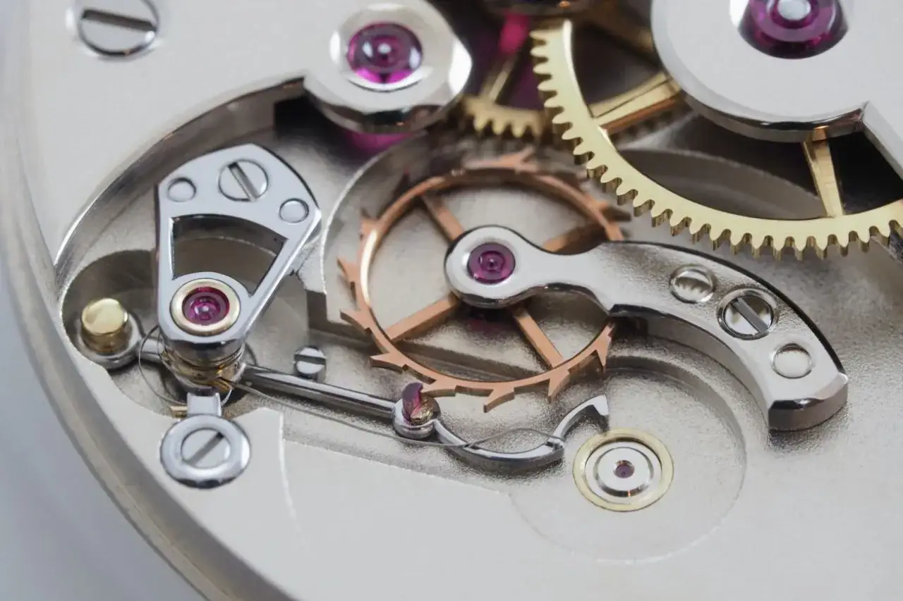 Dettaglio di un meccanismo di orologio con ingranaggi dorati e ruota bilanciere, parte di uno scappamento coassiale.