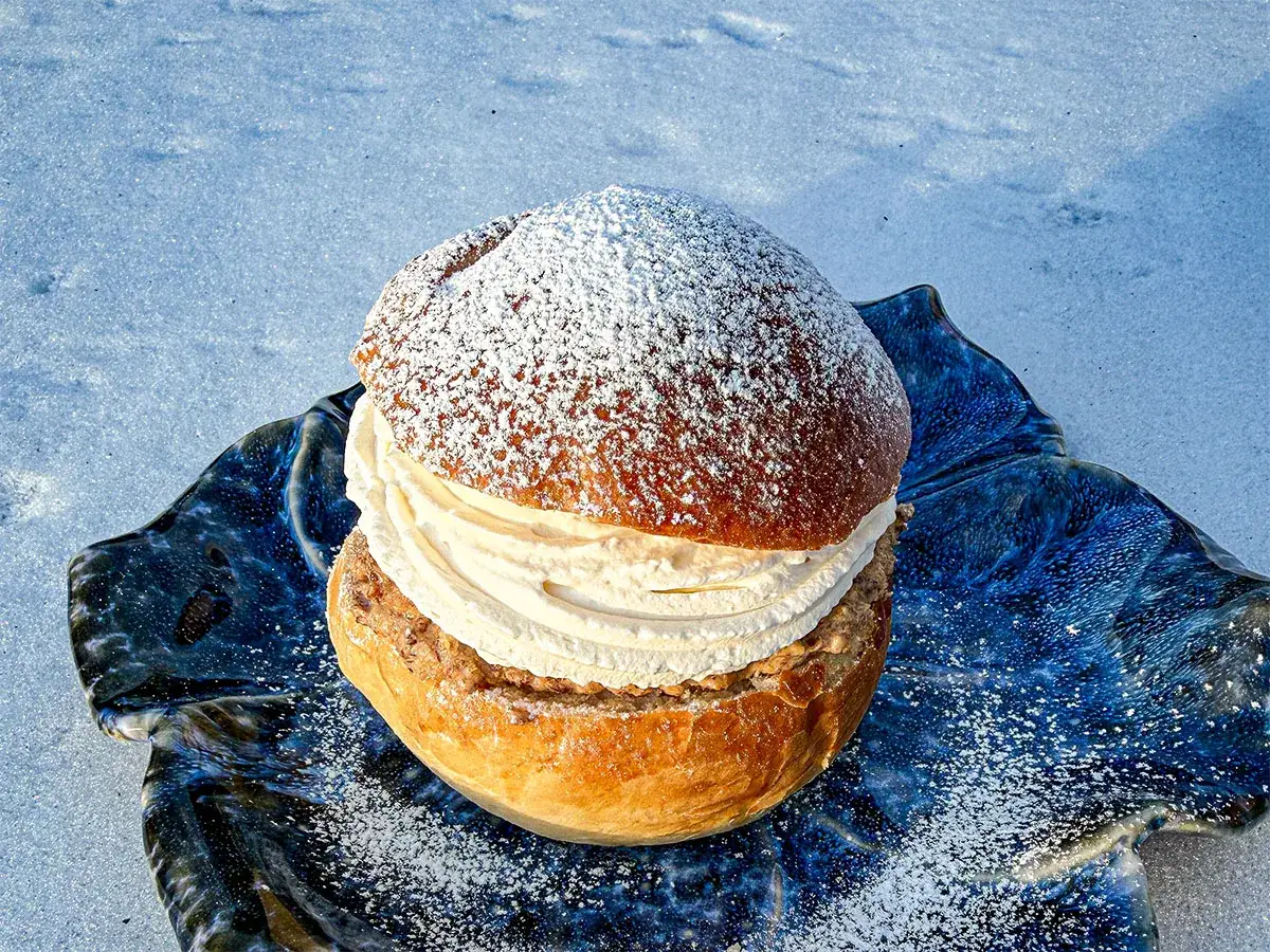 En semla utan mandelmassa, fylld med gr&auml;dde och kardemumma, ligger p&aring; en bl&aring;, v&aring;gig tallrik i sn&ouml;n.