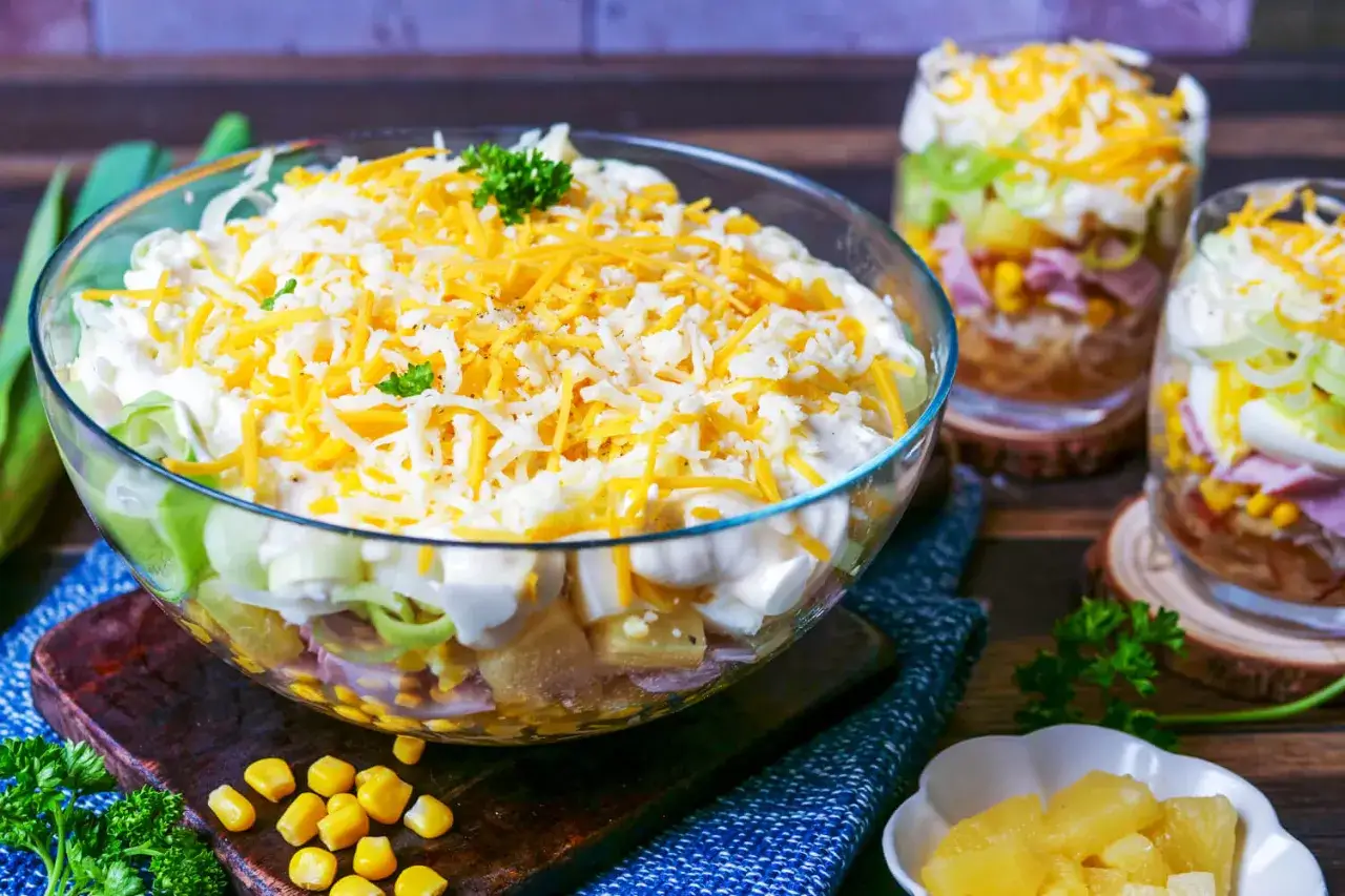 Schichtsalat Rezept: Ein bunter Salat mit Schichten aus Gemüse, Ei, Schinken und Mais, gekrönt mit Käse.