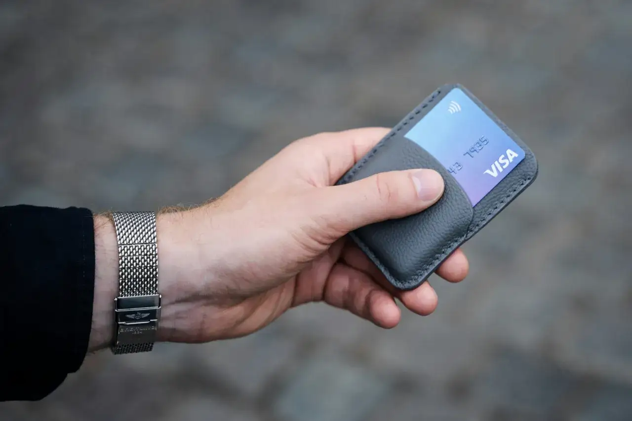 Dłoń trzymająca szary portfel z kartą Visa. To symbol banków, które nie współpracują z komornikiem, zapewniając bezpieczeństwo finansowe.