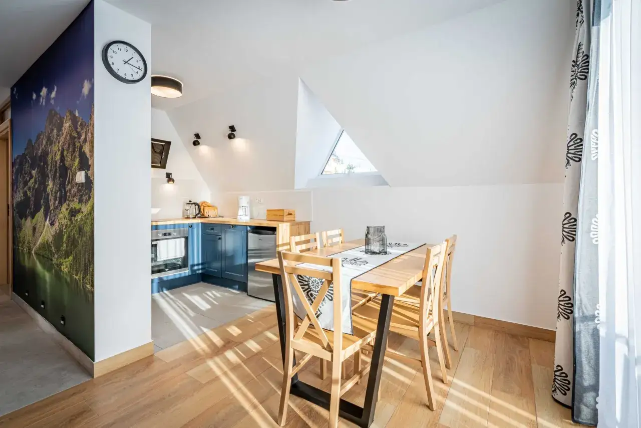 Przytulny apartament pod wierchem z widokiem na góry na fototapecie. Jasna kuchnia, drewniany stół i krzesła.