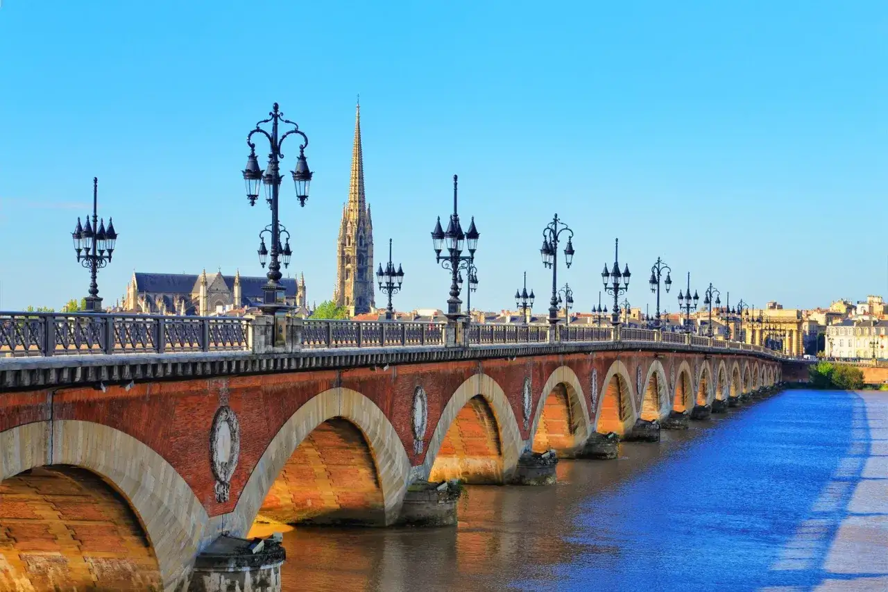 Puente de piedra con farolas y la silueta de la catedral, un clásico que ver en Burdeos.