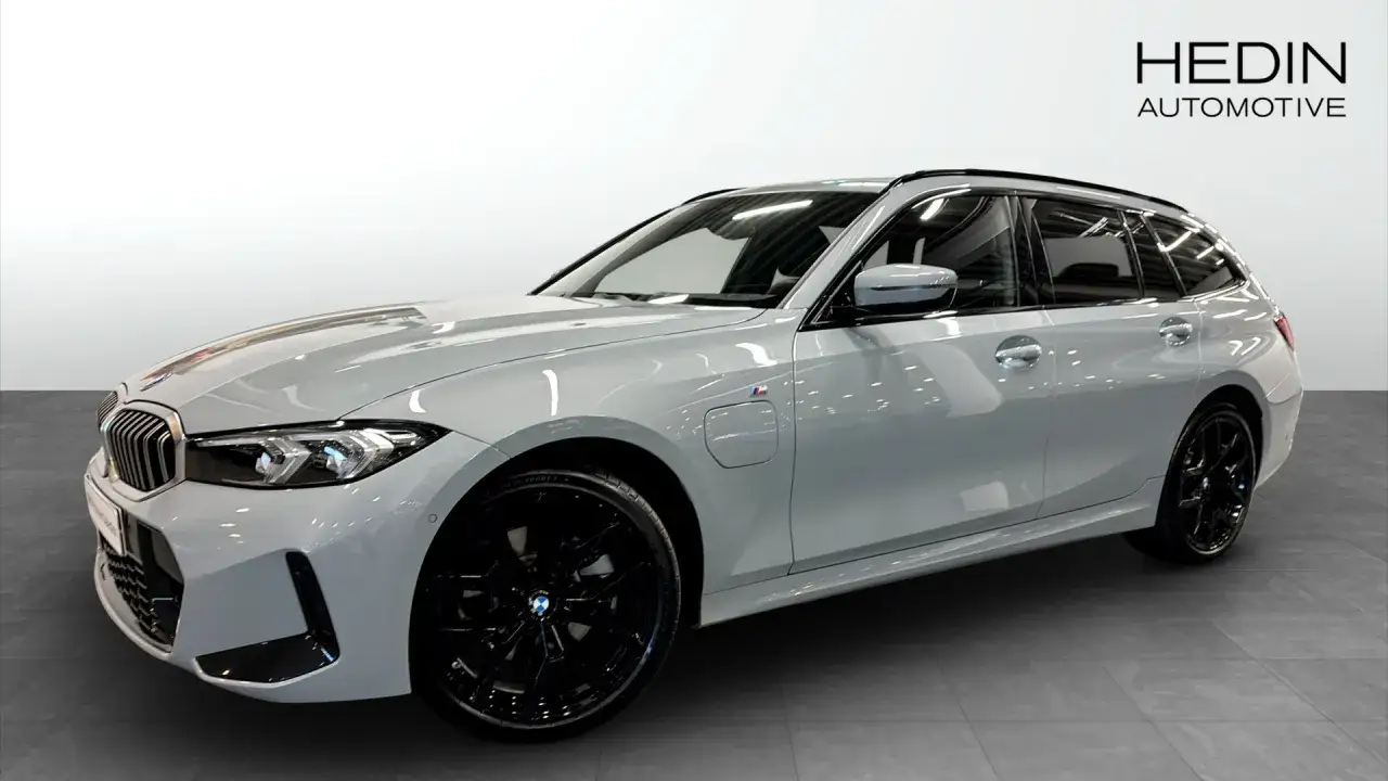 En vit, begagnad BMW 330e kombi med svarta f&auml;lgar st&aring;r i ett showroom.