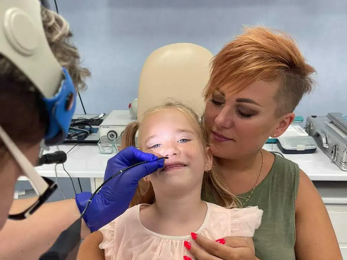 Mama wspiera córkę podczas badania nosa, które może pomóc zdiagnozować przyczynę utraty głosu.