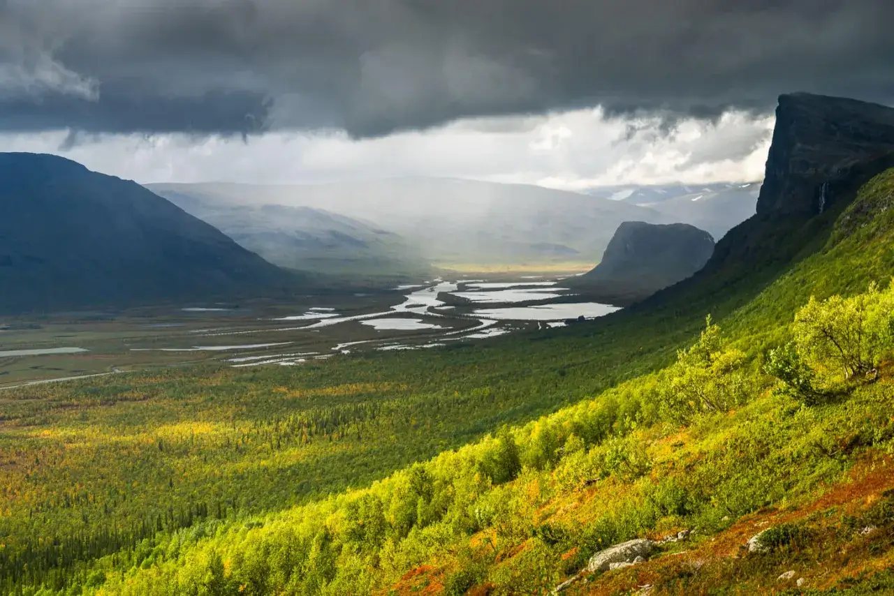Vacker vy &ouml;ver en dalg&aring;ng med slingrande vattendrag och fj&auml;ll i Sarek. Skierfeklippan reser sig majest&auml;tiskt till h&ouml;ger.