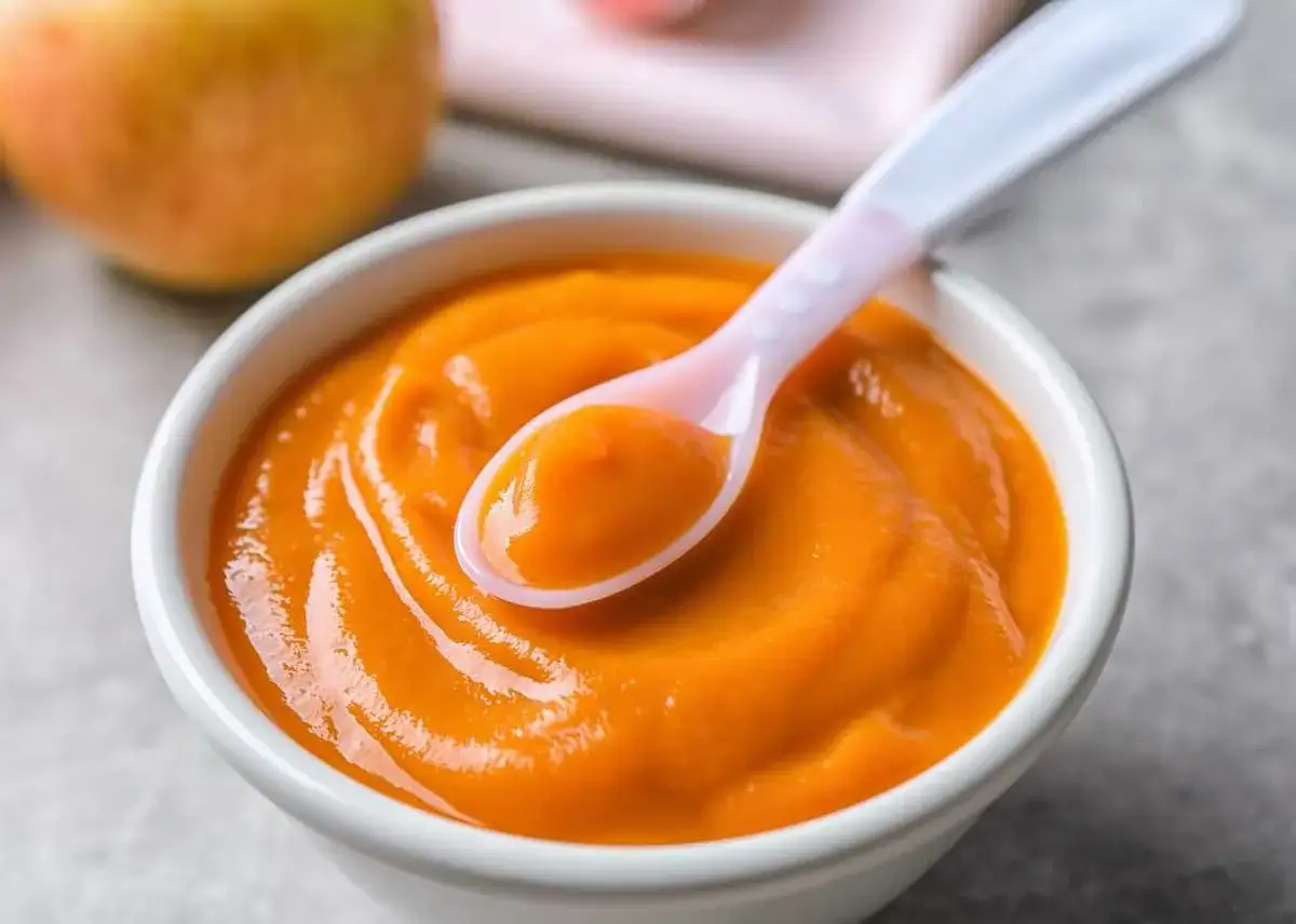Un taz&oacute;n blanco con pur&eacute; de calabaza beb&eacute; y una cuchara rosa con un poco de pur&eacute;.