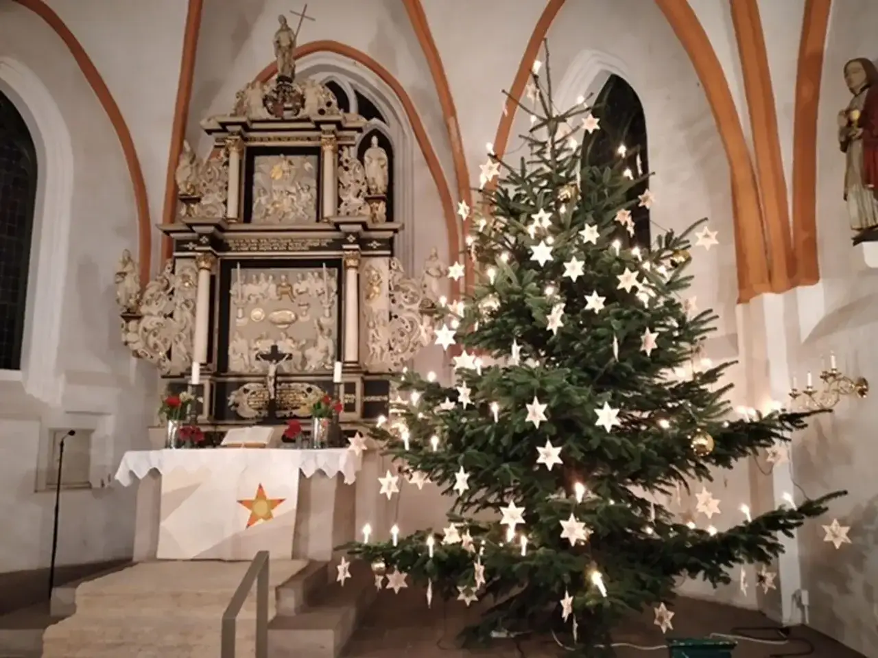 Festlicher Baum mit Sternen und Lichtern im Altarraum einer Kirche, bereit für den evangelischen Gottesdienst am Heiligabend.