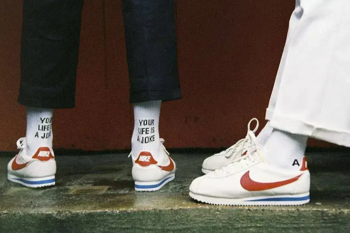 Białe buty Nike Cortez z czerwonym logo i niebieskim paskiem, białe skarpetki z napisem 