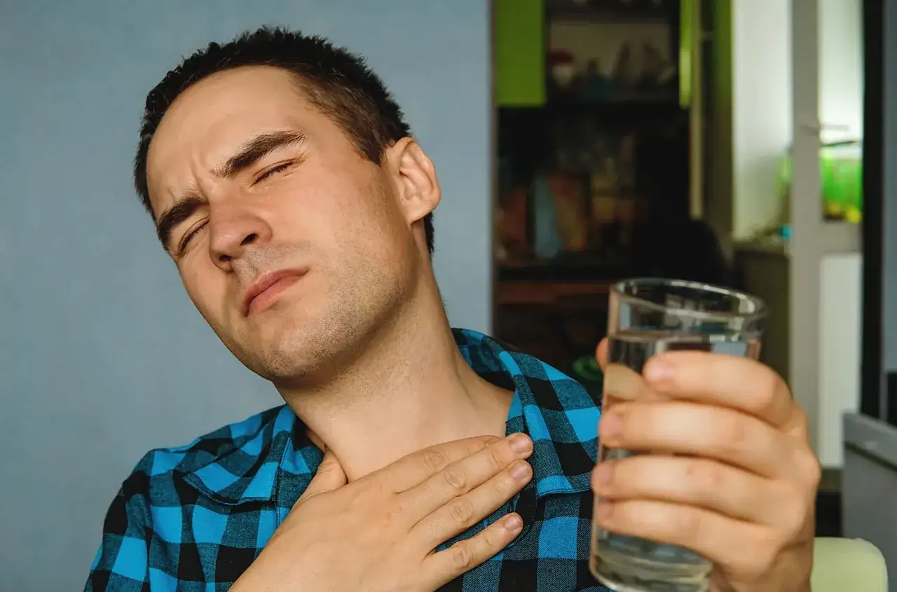 Mężczyzna z bólem gardła, cierpiący na nocny kaszel po alkoholu, sięga po szklankę wody.