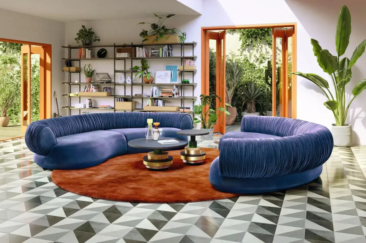 Ein modernes wohnzimmer mit 2 auffälligen, blauen Samtsofas, einem runden Teppich und einem Bücherregal voller Bücher und Pflanzen.