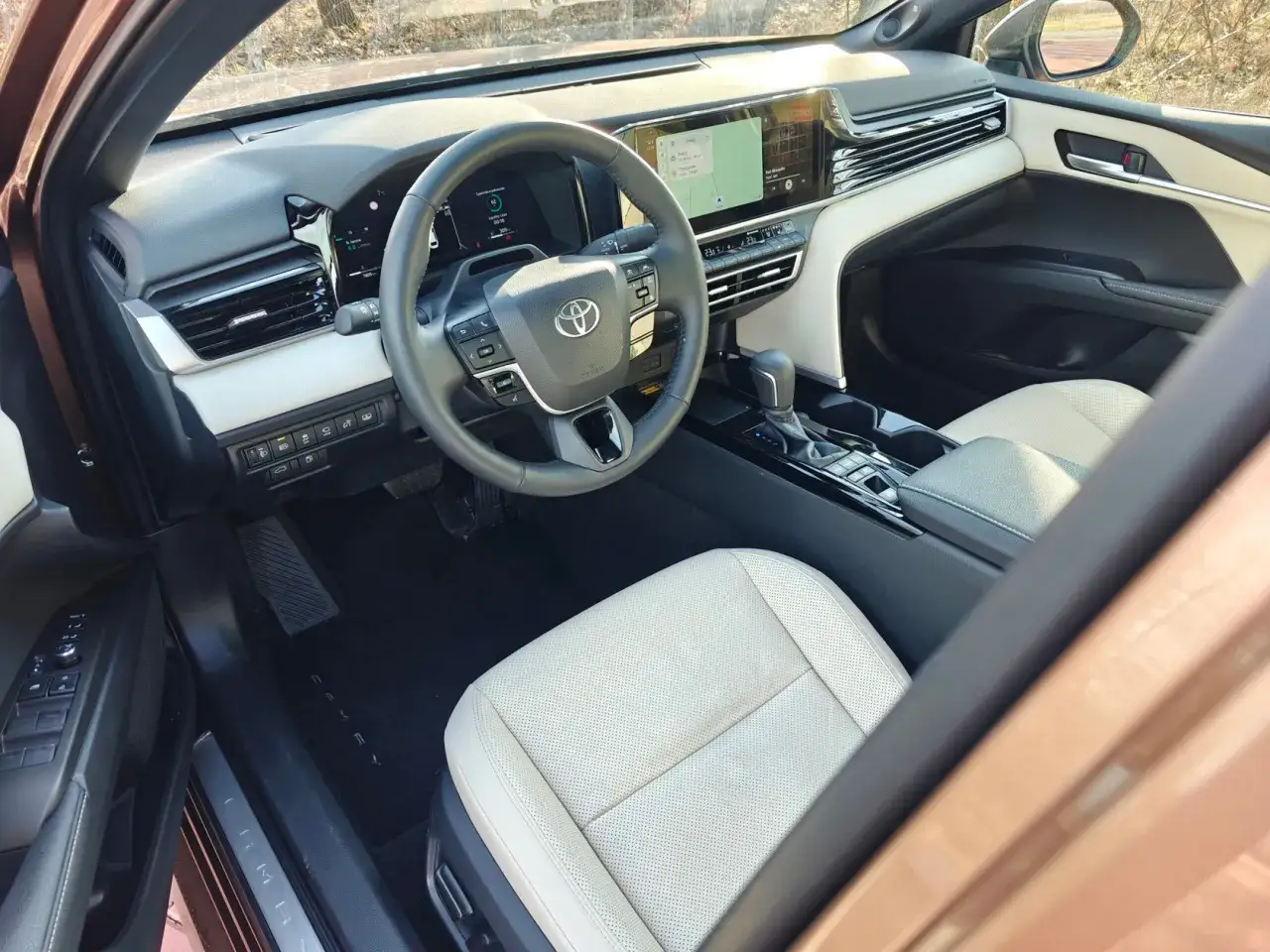 Wnętrze Toyota Camry Hybrid z jasną, skórzaną tapicerką, nowoczesnym ekranem multimedialnym i kierownicą.