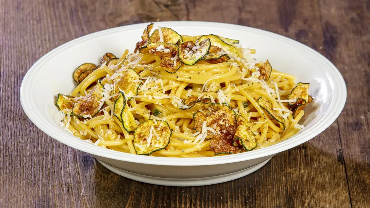 Un piatto invitante di pasta alla nerano ricetta, con spaghetti conditi e guarniti da zucchine fritte croccanti e parmigiano grattugiato.