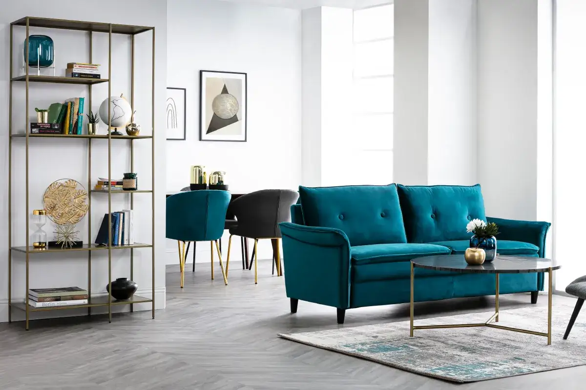Sofá y sillas de terciopelo color petróleo en una sala de estar moderna con estantería dorada y mesa de centro.