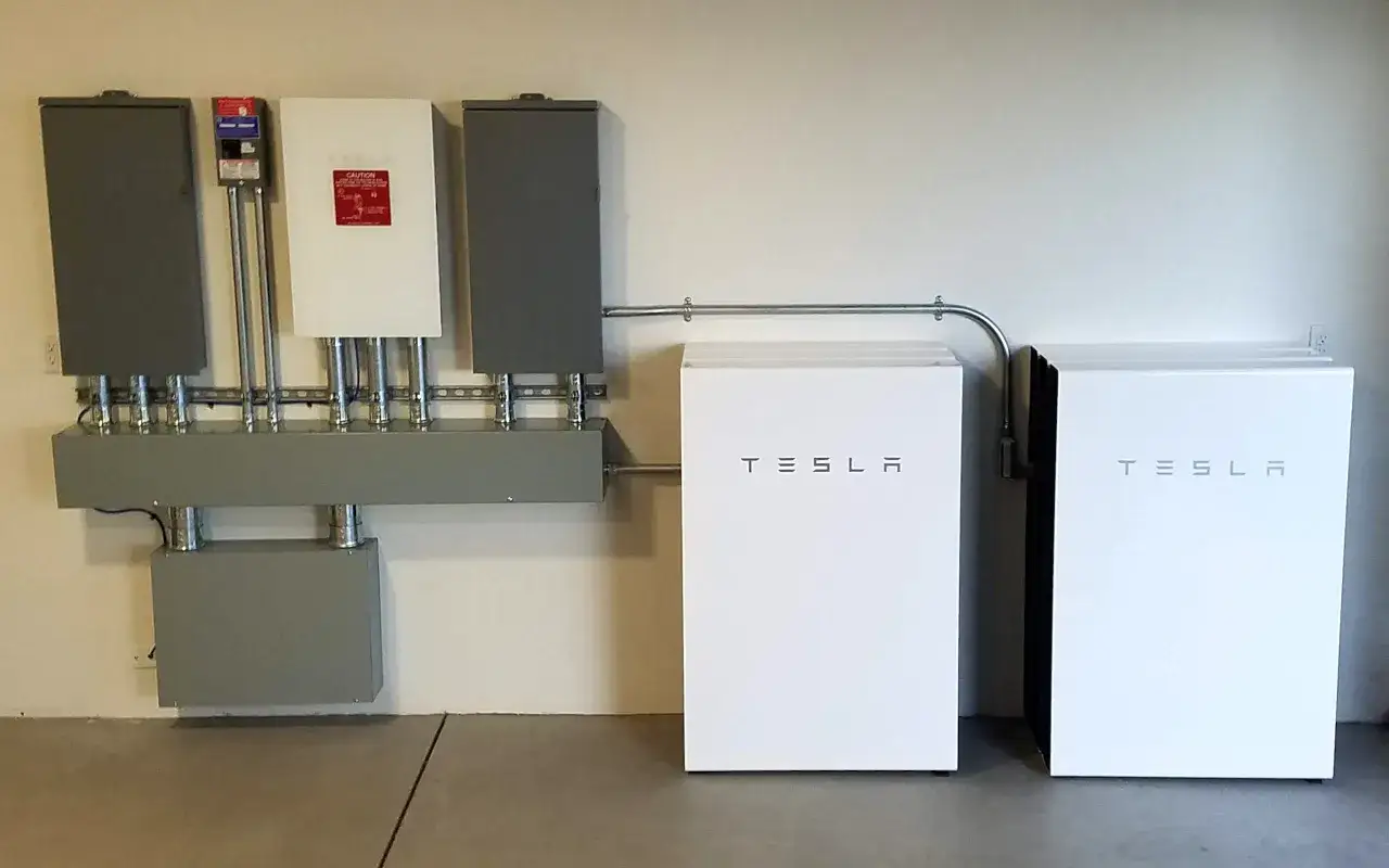 Dwa magazyny energii Tesla obok siebie, z instalacją elektryczną na ścianie. Sprawdź magazyn energii 10kw cena.