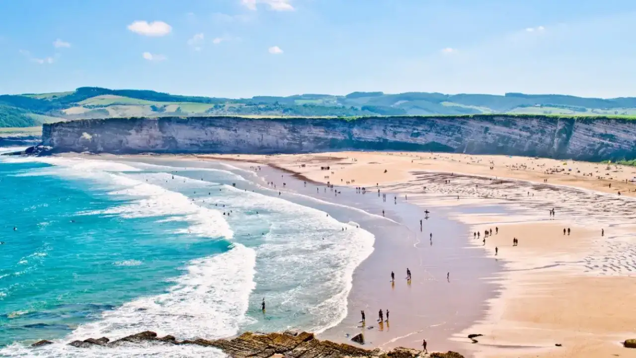 Amplia playa de Cantabria con acantilados, mar turquesa y gente disfrutando del sol y las olas. Un paraíso para las playas nudistas Cantabria.
