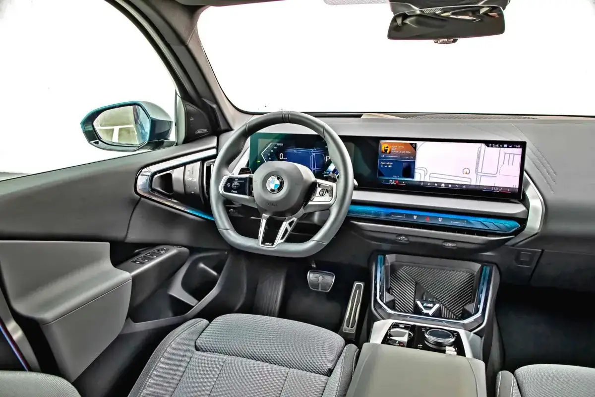 Wnętrze BMW X3 2024 z nowoczesnym kokpitem, dużym ekranem multimedialnym i cyfrowymi zegarami.