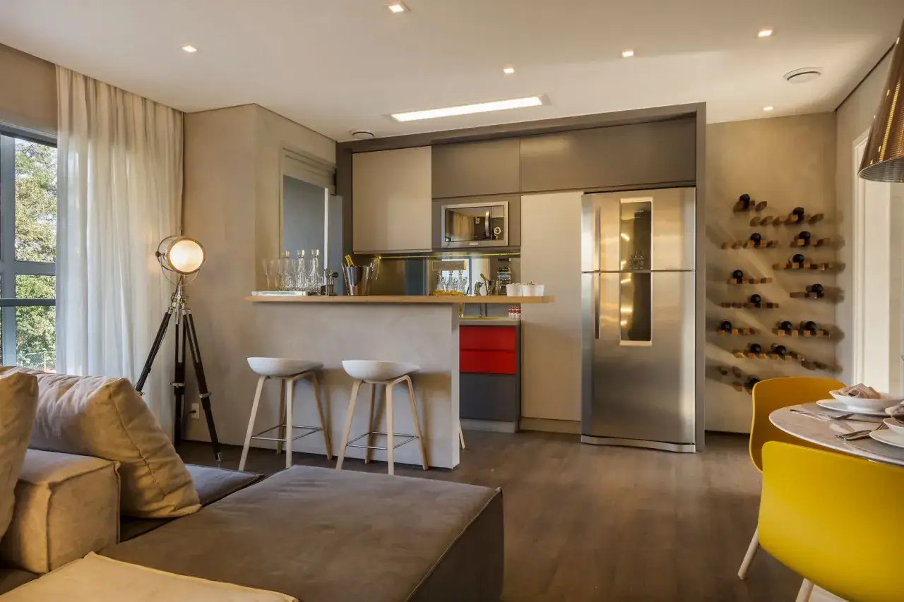 Espacio moderno de cocina salón comedor de 30 m2 con barra, sofás, nevera y estantería de vinos.