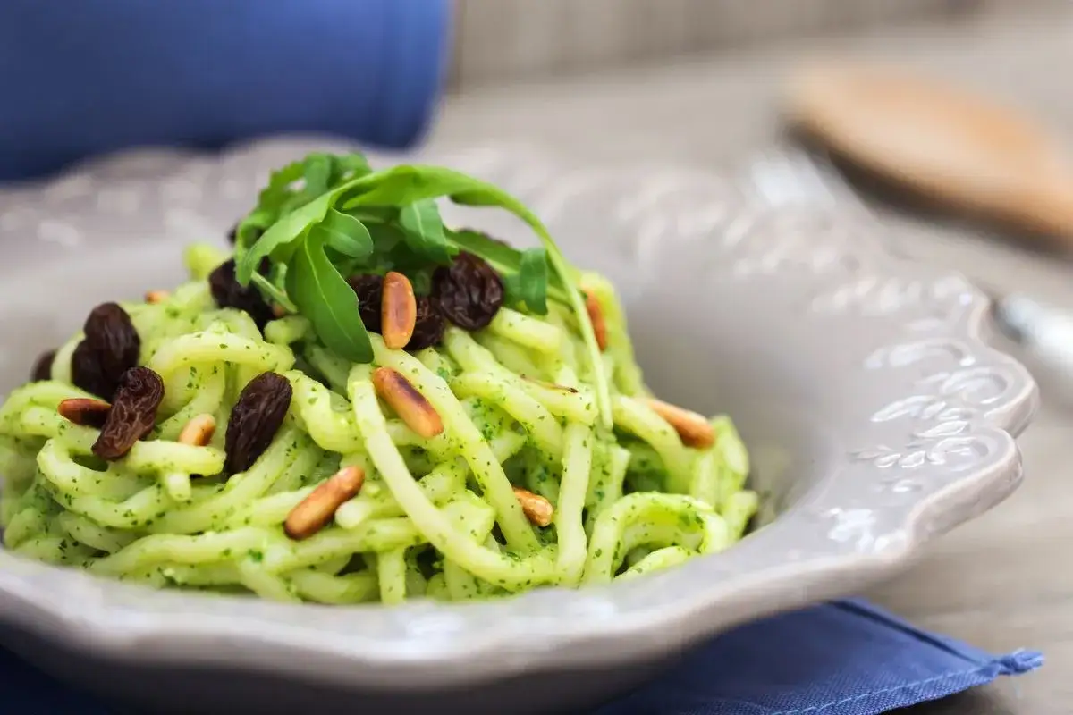 Troccoli pugliesi con condimento verde, uvetta e pinoli tostati, guarniti con rucola fresca.